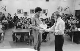 Instructor shaking hand with student in front of a classroom