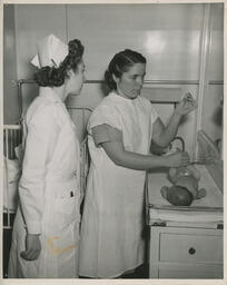 Nurse watches as mother looks at thermometer while holding baby's legs