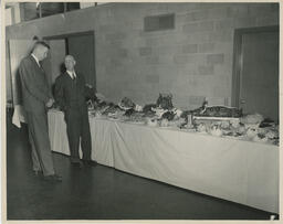 Two administrators look at table with filled with creative dishes, ca. 1949