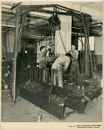 Three students working with chains hanging from ceiling connected to machines, ca. 1960
